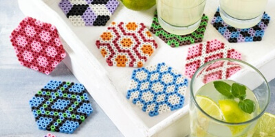 Sommerliche Tischdeko mit bunten Untersetzern und Glasabdeckungen aus Bügelperlen auf einem Serviertablett neben Erfrischungsgetränken