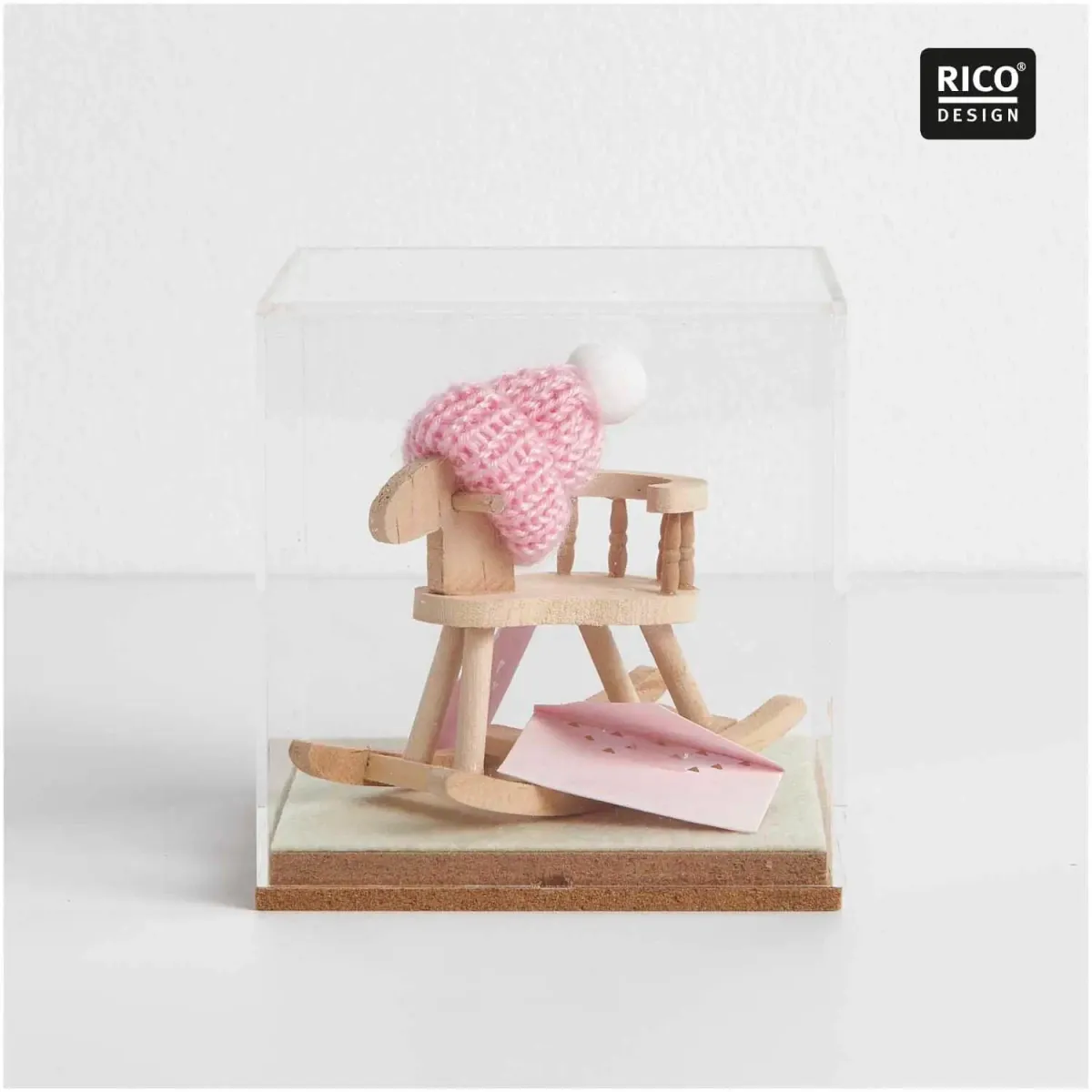 Rosa Miniatur-Strickmütze mit weißer Bommel auf einem Mini-Schaukelpferd unter einer Glashaube als liebevoll gestaltete Geschenkdekoration