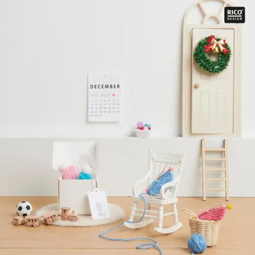 Rosa und hellblaue Miniatur-Strickmützen mit weißen Bommeln neben Miniatur-Strickzeug in einer Wichteltür-Szene