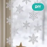 Winterliche Fensterdeko mit ausgestanzten Schneeflocken aus verschiedenen Papieren, die an feinen Fäden vor dem Fenster hängen und wie fallender Schnee wirken